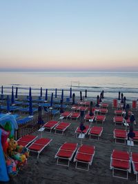 Empty lounge chairs at beach against clear sky during sunset