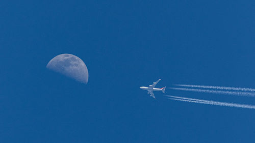 Full frame view of a jet airplay flying towards the moon against a clear blue sky