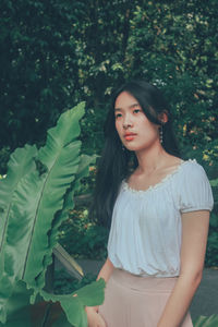 Portrait of a beautiful young woman standing against plants