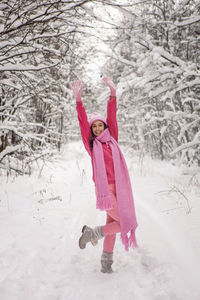 Woman raise your hands up. woods in pink clothes a jacket a knitted scarf. snowy forest in winter