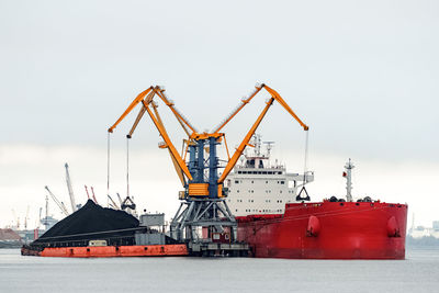 Cranes at commercial dock against sky