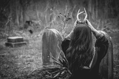 Rear view of woman holding antlers on head over field at graveyard