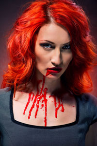 Young redhead woman with blood standing against wall