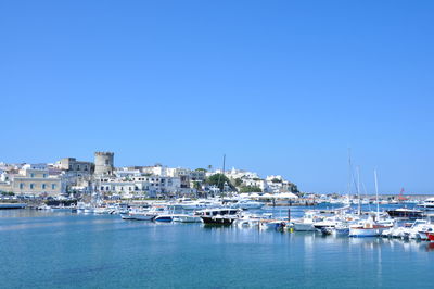 Sailboats moored in harbor by buildings against clear blue sky