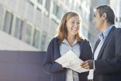 Smiling businesspeople discussing over document outside office building