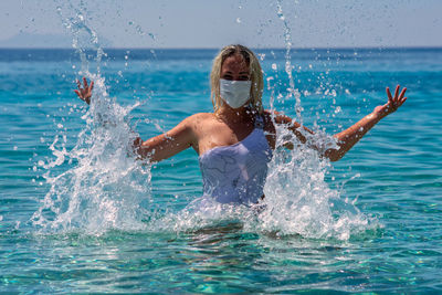 Woman wearing facemask enjoying in swimming pool against sea