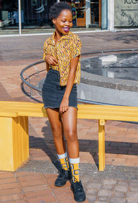 Full length of smiling young woman standing against seat