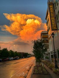 Road by buildings against sky during sunset