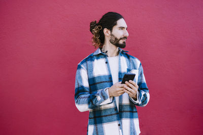 Young man using mobile phone against wall