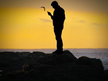 Silhouette man standing on rock at beach during sunset