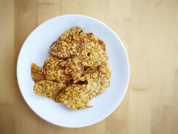 Fried tempeh in a white plate on the wooden surface.