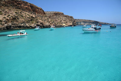 Boats in sea against clear blue sky