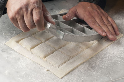 Cropped hands of chef cutting dough on table in commercial kitchen