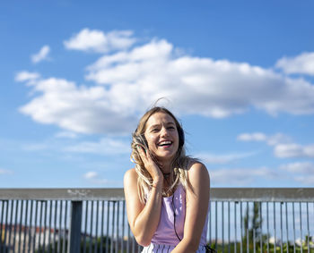 Smiling young woman listening to music against sky