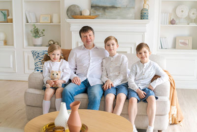 Happy father with three little children sitting on sofa looking at each other