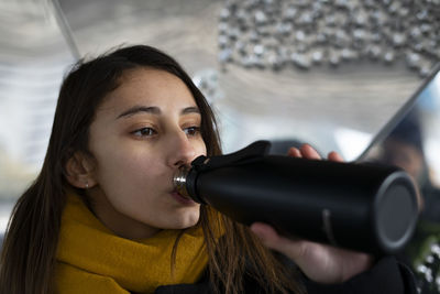 Young woman drinking water from a black thermos.