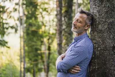 Side view of man on tree trunk in forest