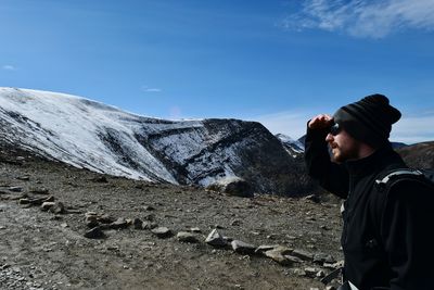 Side view of male hiker shielding eyes at mountain against blue sky on sunny day