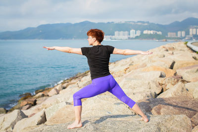 Rear view of woman practicing yoga on rocky shore