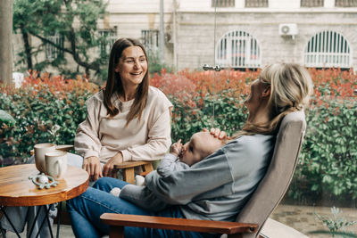 Portrait of smiling friends using phone while sitting at park