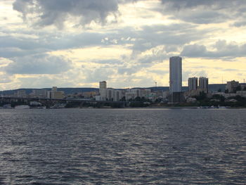 Sea by buildings against sky during sunset