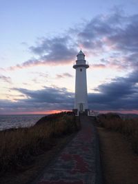 Footpath leading towards lighthouse by sea during sunset