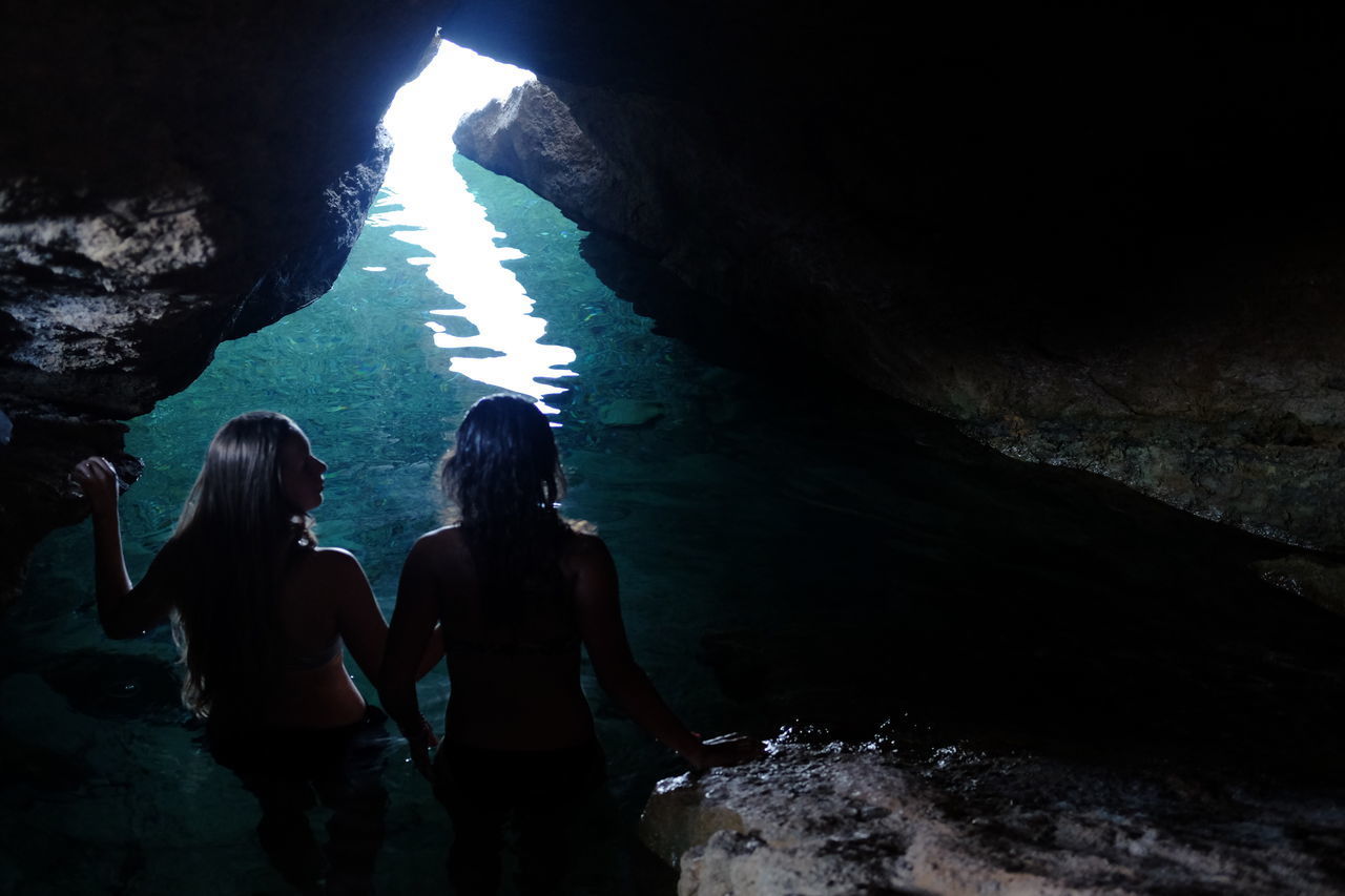 REAR VIEW OF WOMEN STANDING ON ROCK AT CAVE