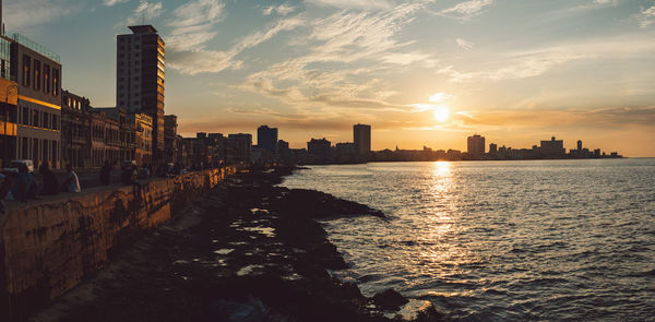 Buildings by sea against sky during sunset