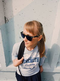 Full length of woman wearing sunglasses standing against wall