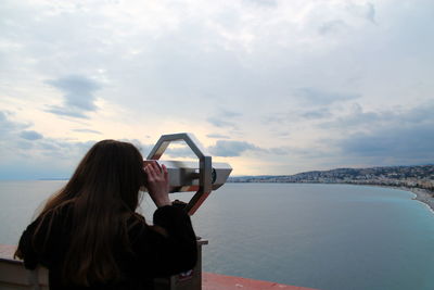 Rear view of woman looking through telescope against sea and sky