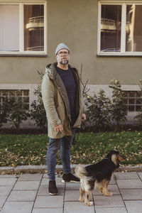 Full length portrait of man standing with dog on footpath in city