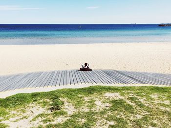 Man sitting on shore at beach against sky