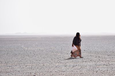 Woman walking at desert against sky