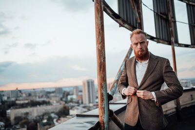 Portrait of young man standing in city against sky