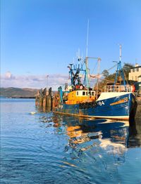 Fishing boats moored at harbor against clear blue sky