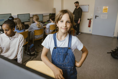 Portrait of smiling girl standing with hand on hip in computer classroom at office