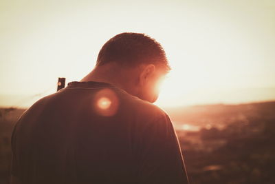 Rear view of boy standing against sky during sunset