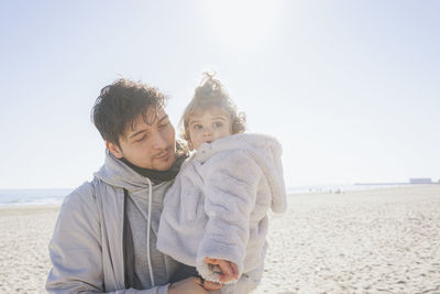 Smiling father with daughter standing at beach on sunny day