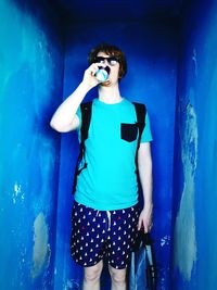 Portrait of young woman standing against blue wall