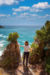 Rear view of woman standing at beach against sky