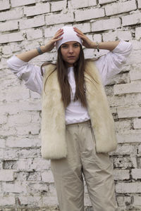 Portrait of young woman standing against brick wall