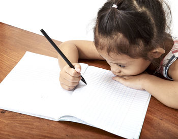 High angle view of girl writing on book at desk against white background