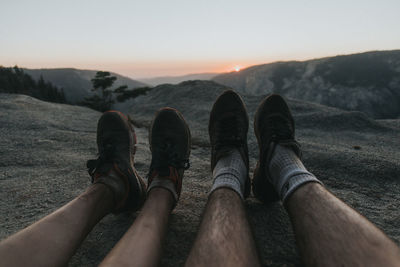 Low section of men relaxing on mountain against sky during sunset