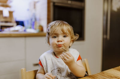 Close-up portrait of cute baby girl eating cookie at home