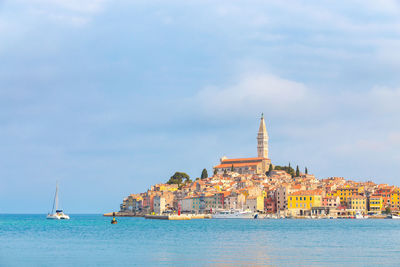 Sailboats in sea by buildings against sky