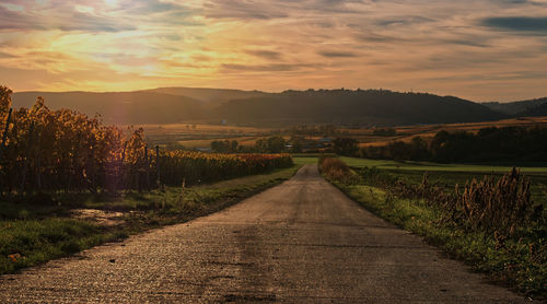 Empty road amidst field against sky during sunset