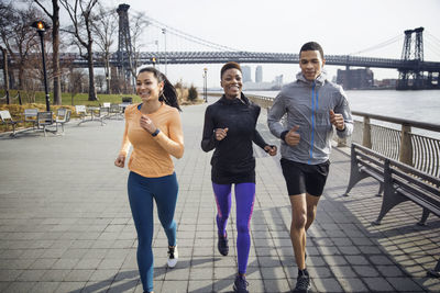 Happy multi-ethnic athletes running on footpath with williamsburg bridge in background