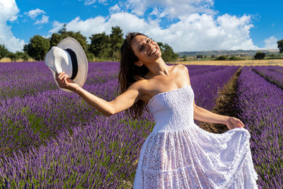 Portrait of a happy young woman playing with her hat in a blooming lavender field. 