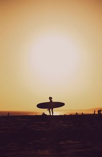 Silhouette man with surfboard on beach at sunset