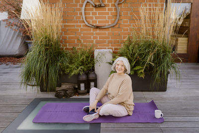 Portrait of smiling senior woman sitting on exercise mat at terrace